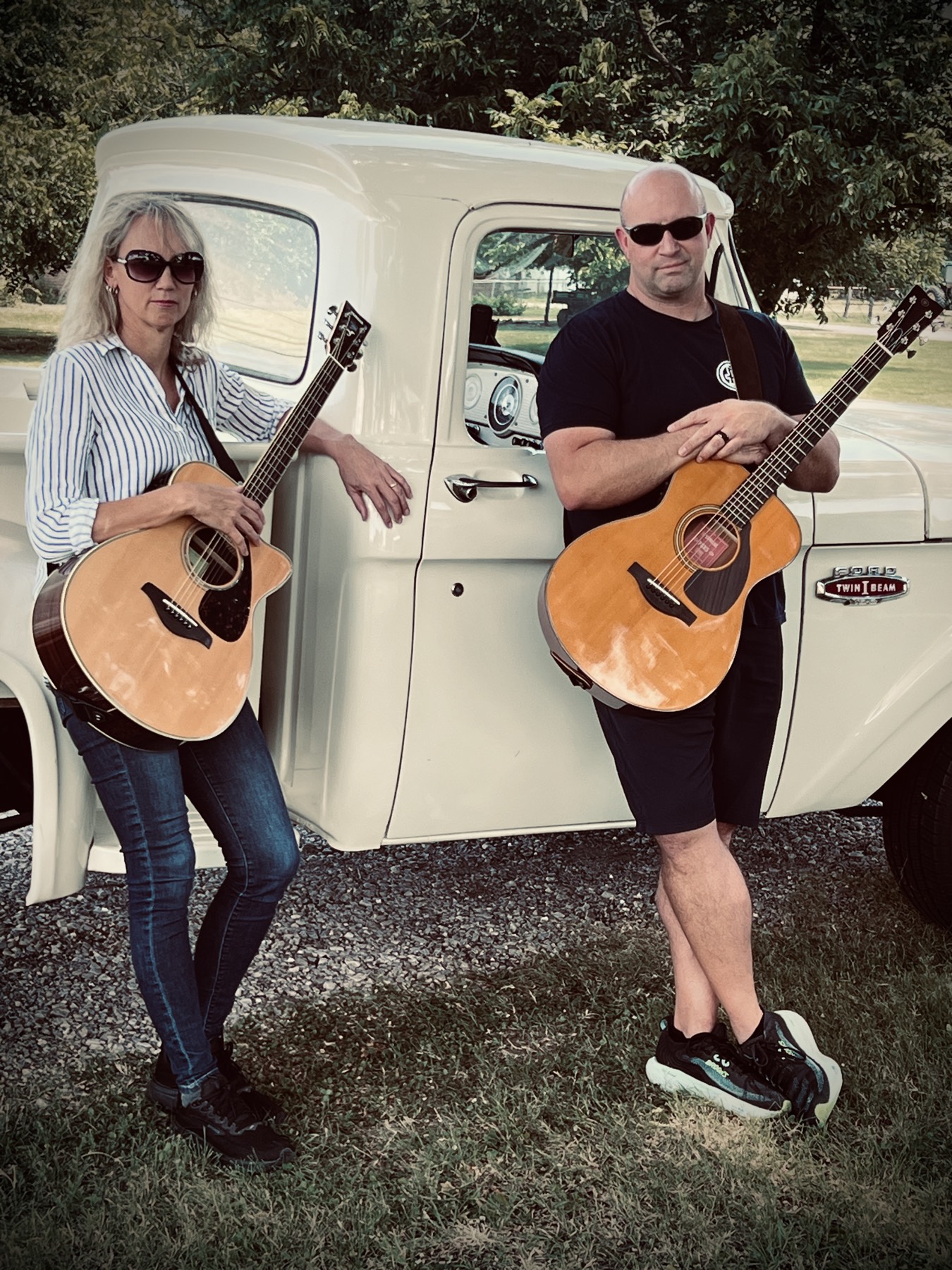 Rebekah Johnson and Steve Horvath holding acoustic guitars in front of a vintage Ford pickup truck